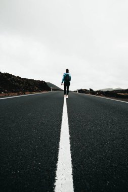 Kadın turist (sırt çantalı) ve bulutlu bir günde mükemmel simetrik çizgiler olan boş yolun dikey görüntüsü. Lav Adası 'ndan Lanzarote (Kanarya Adaları)).  