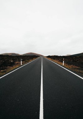 Bulutlu bir günde mükemmel simetrik çizgileri olan boş yolun dikey görüntüsü. Lav Adası 'ndan Lanzarote (Kanarya Adaları)). 