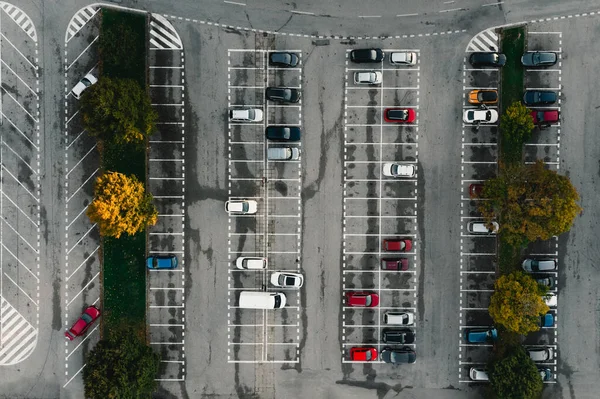 stock image Parking lot and parked colorful cars between the lines from above (top view) - grey concrete background. Parking lot with colorful trees in autumn season.