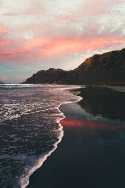 Lanzarote, Kanarya Adaları 'ndaki Famara Sahili' nin altın saatindeki güzel gelgit manzarası. Sahilde gün batımının fotoğrafı. Okyanusun yansıması, pembe gökyüzü ve arka planda uçurum..