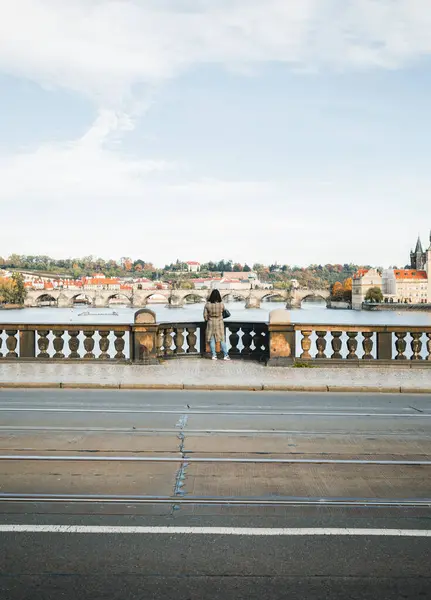 Prag 'da (Çek Cumhuriyeti) Vltava nehrinin üzerindeki köprüde duran gri paltolu kadın gezgin, Charles Bridge' e arkadan bakıyor. Şehirdeki kadın turistin geniş açı çekimi..