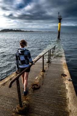 Brittany, Fransa 'nın Finistere Atlantik Sahili' ndeki Roscoff şehrinde bulunan Ile De Batz 'e giden köprünün sonundaki genç kadın.