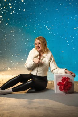 Sarışın, beyaz kürklü, mavi arka planda beyaz kazaklı beyaz bir kadın. Sahte Kar her tarafına akıyor. O mutlu, yeni yılı ve Noel 'i bir hediyeyle kutluyor. Stüdyo resmi