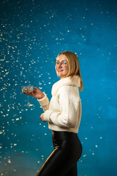 穿着蓝色背景的白色毛皮毛衣的金发美女 假雪在她身上飞舞 她很高兴 庆祝圣诞节和新年 工作室肖像 — 图库照片