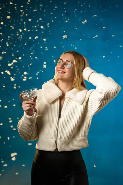 青い背景に白い毛皮のセーターのブロンドかわいい慎重な女性 偽の雪が彼女の上を流れています 彼女は幸せで クリスマスと新年を祝います スタジオポートレート ストックフォト