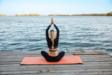 Genç ve güzel bir kız, nehrin kıyısında sakin ve sıcak bir akşamda yoga yapıyor..