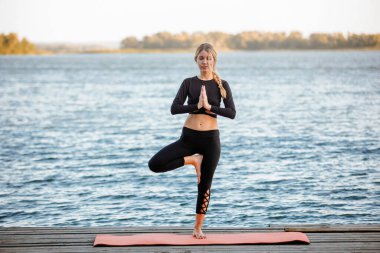 Genç ve güzel bir kız, nehrin kıyısında sakin ve sıcak bir akşamda yoga yapıyor..
