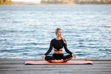 Genç ve güzel bir kız, nehrin kıyısında sakin ve sıcak bir akşamda yoga yapıyor..