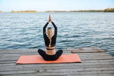 Genç ve güzel bir kız, nehrin kıyısında sakin ve sıcak bir akşamda yoga yapıyor..