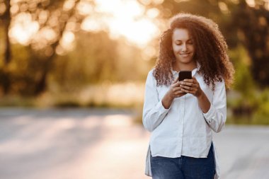 A young girl walks in the park and uses social networks using a mobile phone.