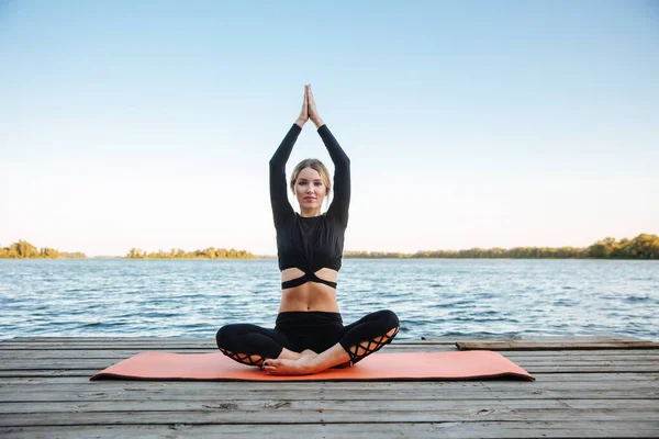 stock image A young beautiful girl is doing yoga in a calm warm evening on the banks of the river.