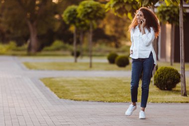 A young girl walks in the park and uses social networks using a mobile phone.