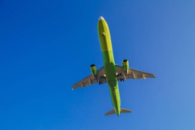 Passenger plane of yellow-green color flies in the blue sky, air transportation concept, population evacuation.