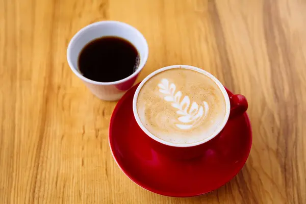 红色杯子中的芳香咖啡 有牛奶泡沫和拿铁艺术 新鲜煮好的咖啡 白色杯子 放在轻薄的木制桌子上 咖啡的选择 — 图库照片