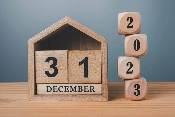 Wooden blocks lined up with 2023 numbers and wooden house on December 31st, last day of the year goal concept.