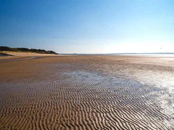 Galler 'in Burry Limanı' ndaki kumlu sahile bak. Dalgaların çekildiği yerde tırmık izleri var.