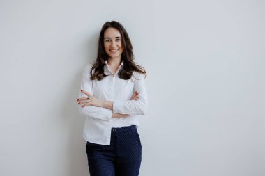 Genç bir kadın kollarını tarafsız bir duvara çarpmış şekilde poz veriyor. Gıcır gıcır beyaz bir bluz ve denizci pantolonu giyiyor, kendine güveni ve sıcaklığıyla gülümsüyor..