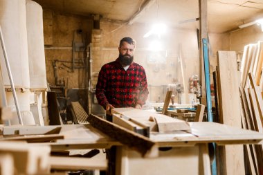 Becerikli bir marangoz, aletler ve ahşap parçalarıyla dolu işlek bir marangozhanedeki işine odaklanır ve iyi aydınlatılmış bir çevrede sanatına olan bağlılığını gösterir..