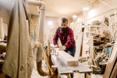 Yetenekli bir marangoz, ahşap işçiliği atölyesinde, ahşap talaşı ve kereste talaşı ile çevrili iken, hassas aletlerle ahşap bir kalas şekillendirir..