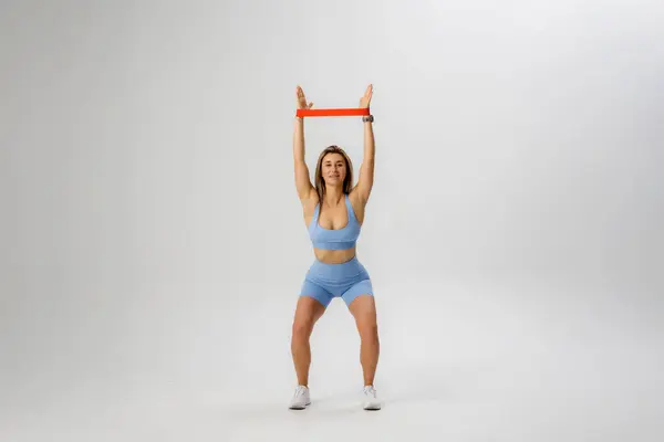 Bir kadın, sabit bir pozisyonda otururken bir direniş bandını yukarıda tutarak fitness aktivitesiyle meşgul oluyor..