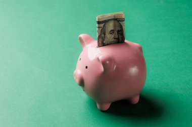 Pembe bir kumbarada tasarruf ve mali sorumluluğun önemini sembolize eden katlanmış bir banknot var. Parlak yeşil arkaplan tasarruflara odaklanmayı artırır.