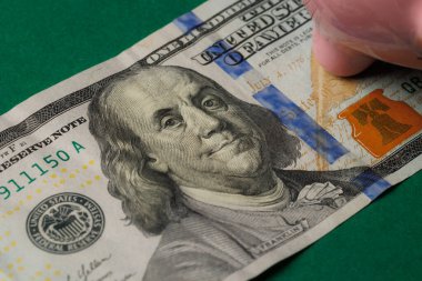 Benjamin Franklins 'in portresini gösteren yüz dolarlık banknotun detaylı görüntüsü. Köşede bir kumbara var. Finansal planlama oturumu sırasında yeşil bir yüzey üzerinde dinleniyor..