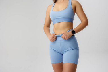 Açık mavi kıyafetli sporcu antrenmana hazırlanıyor. Atletik duruşları ve kıyafetleri üzerinde duruluyor. Stüdyo, etkinliği vurgulamak için dağınık ve nötr bir arka plana sahiptir..