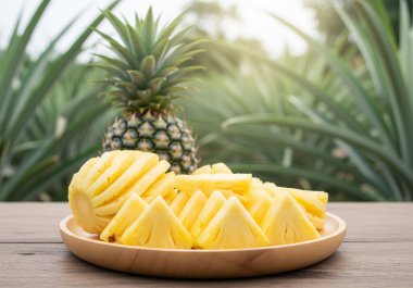 Taze, soyulmuş ve dilimlenmiş ananas parçalarıyla dolu ahşap bir tabak, arka planda bütün bir ananas, rustik ahşap bir masa üzerine kurulmuş..