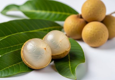 Taze hasat edilmiş Longan meyvesi. Bazıları şeffaf eti göstermek için soyulmuş. Yeşil yapraklar üzerinde sergilenmiş..