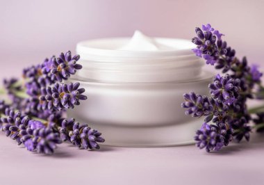 Lavanta çiçekleriyle dolu berrak bir kavanozda beyaz krem. Cilt için nazik ve aromatik bir bakım öneriyor..