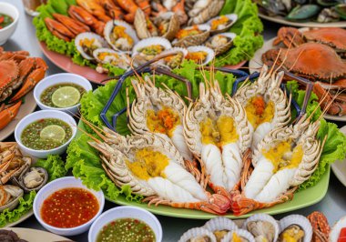 Büyük nehir karidesleri, yengeçler ve istiridyeler de dahil olmak üzere çeşitli taze ızgara ve buharda pişmiş deniz ürünleriyle dolu müsrif bir tabak taze marul yatağında çeşitli baharatlı soslarla servis ediliyor..