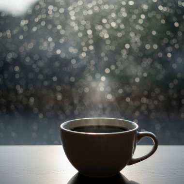 Yağmurlu gün tesellisi: Sıcak bir içeceğin keyfini çıkarmak, pencere camından süzülen yağmur damlaları, barışçıl ve iç gözlemci bir atmosfer yaratıyor..