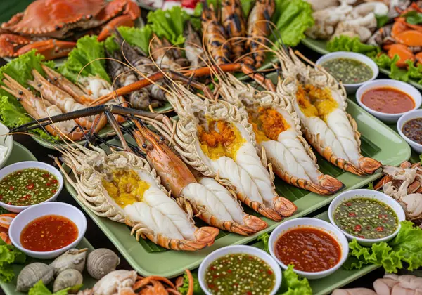 Büyük nehir karidesleri, yengeçler ve istiridyeler de dahil olmak üzere çeşitli taze ızgara ve buharda pişmiş deniz ürünleriyle dolu müsrif bir tabak taze marul yatağında çeşitli baharatlı soslarla servis ediliyor..