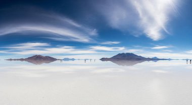 Bolivya 'nın Salar de Uyuni' sinin gerçeküstü manzarası. İnce bir su tabakası gökyüzünü ve uzak volkanları mükemmel yansıtıyor ve nefes kesici bir ufuk oluşturuyor..