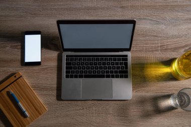 Ofisteki ahşap masada dizüstü bilgisayar ve akıllı telefon manzarası.