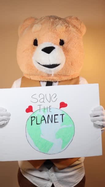 一个头戴泰迪熊黄色背景的人拿着一个标牌 上面写着 拯救地球 正确的视频 — 图库视频影像