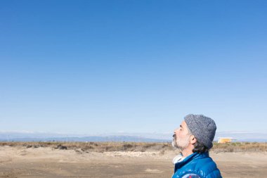 Rahatlamış bir adam, arka planda mavi gökyüzü olan dağların yakınında temiz hava soluyor.