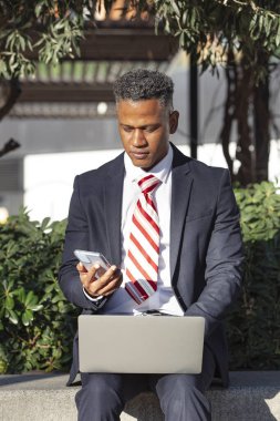 Front view of a handsome businessman working remotely in the city park