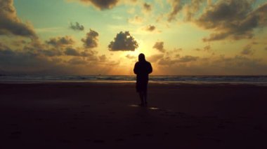 Sahilde yalnız bir adamın silueti. Gün batımında sahilde yürüyen yalnız bir turist manzarası..