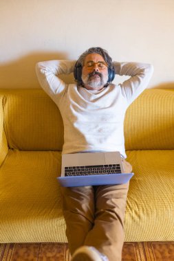 Kanepede oturan ve kulaklık takan olgun bir adamın portresi.