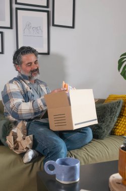 İnternetten alışveriş yaptıktan sonra evde boks paketini açan mutlu bir adam.