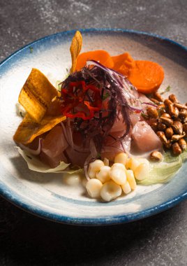 Balık, mısır, tatlı patates, kırmızı soğan, deniz yosunu, kızarmış muz ve kanka içeren taze ceviche tabağı zarif mavi ve beyaz bir tabakta servis edilir.