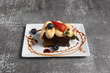 Çikolatalı pasta dilimi dulce de leche cream, taze çilek, yaban mersini, karamel sosu ve bir tutam tarçın ile süslenir.