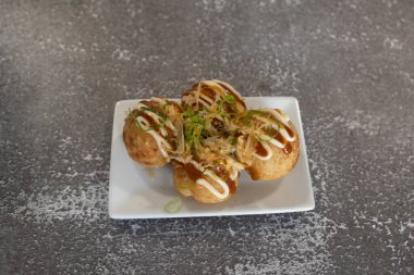 Sos ve yeşil soğanla süslenmiş lezzetli takoyaki topları.