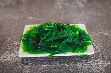 Gri masa üstünde baharatlı yosun salatası içeren küçük beyaz tabak.