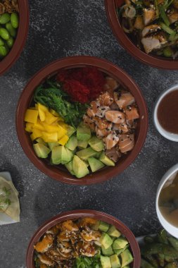 Değişik taze malzemelerle dolu renkli dürtme kaseleri koyu dokulu bir masaya dizilir ve canlı ve iştah açıcı bir görüntü oluşturur.