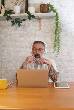 Kulaklıklı bir adam evde dizüstü bilgisayarla çalışıyor.