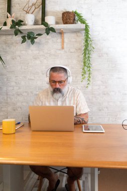 Ev ofisinden bilgisayar ve dijital tablet kullanarak çalışan kulaklık takan sakallı bir serbest çalışan.
