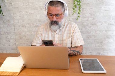 Sakallı adam uzaktan kumandalı aletlerle tahta bir masada çalışıyor.