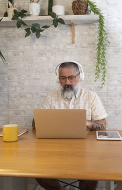 Evde dizüstü bilgisayar ve kulaklık kullanarak çalışan, rahat ve verimli uzaktan çalışma ortamının keyfini çıkaran olgun bir serbest çalışan.